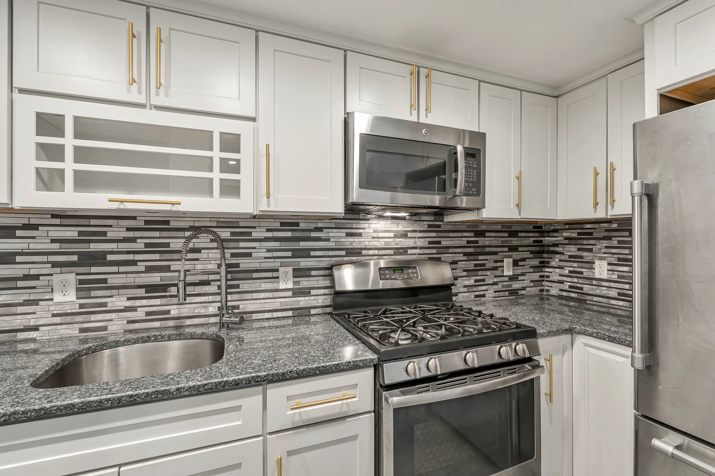 Stainless gas range, microwave, and sink with a mosaic backsplash in the Apartment B kitchen.