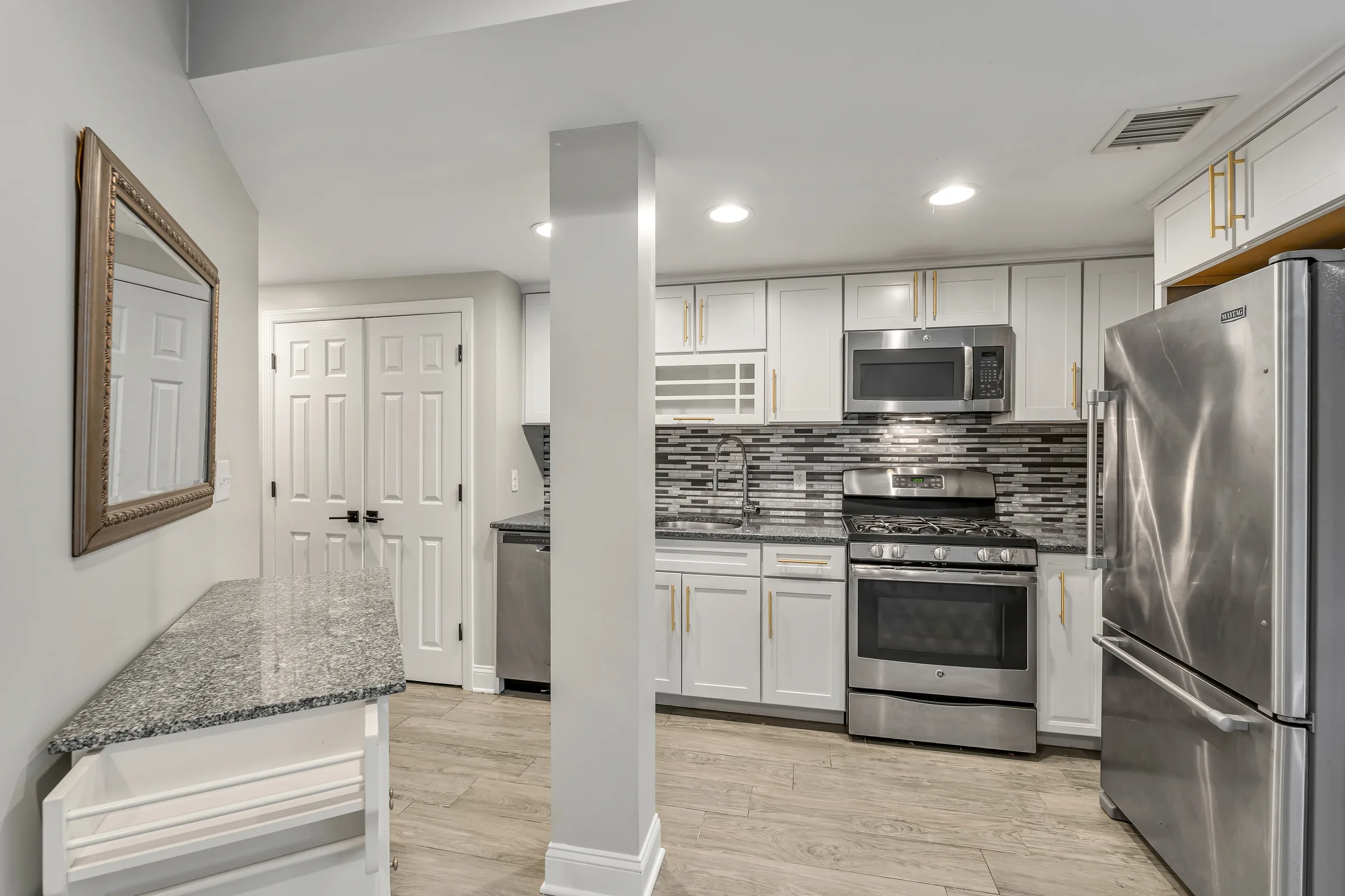 Garden apartment kitchen with stainless steel appliances, white cabinets, and granite counters, Uptown Hoboken.