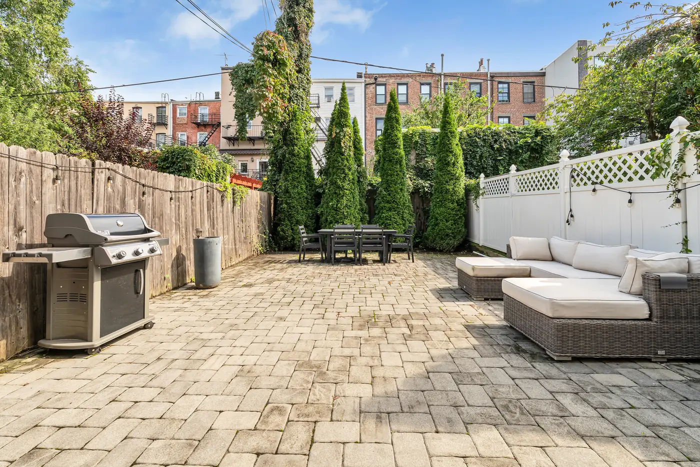 Paver patio with a grill and tall evergreens at 829 Garden Street, Uptown Hoboken.