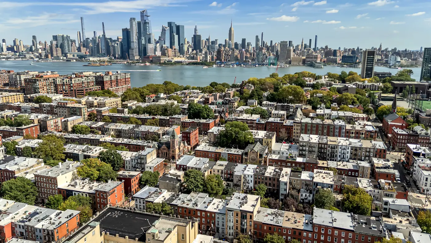 Aerial view of Uptown Hoboken rooftops, the Hudson River, and the Midtown Manhattan skyline, including the Empire State Building, above the garden patio at 829 Garden Street.