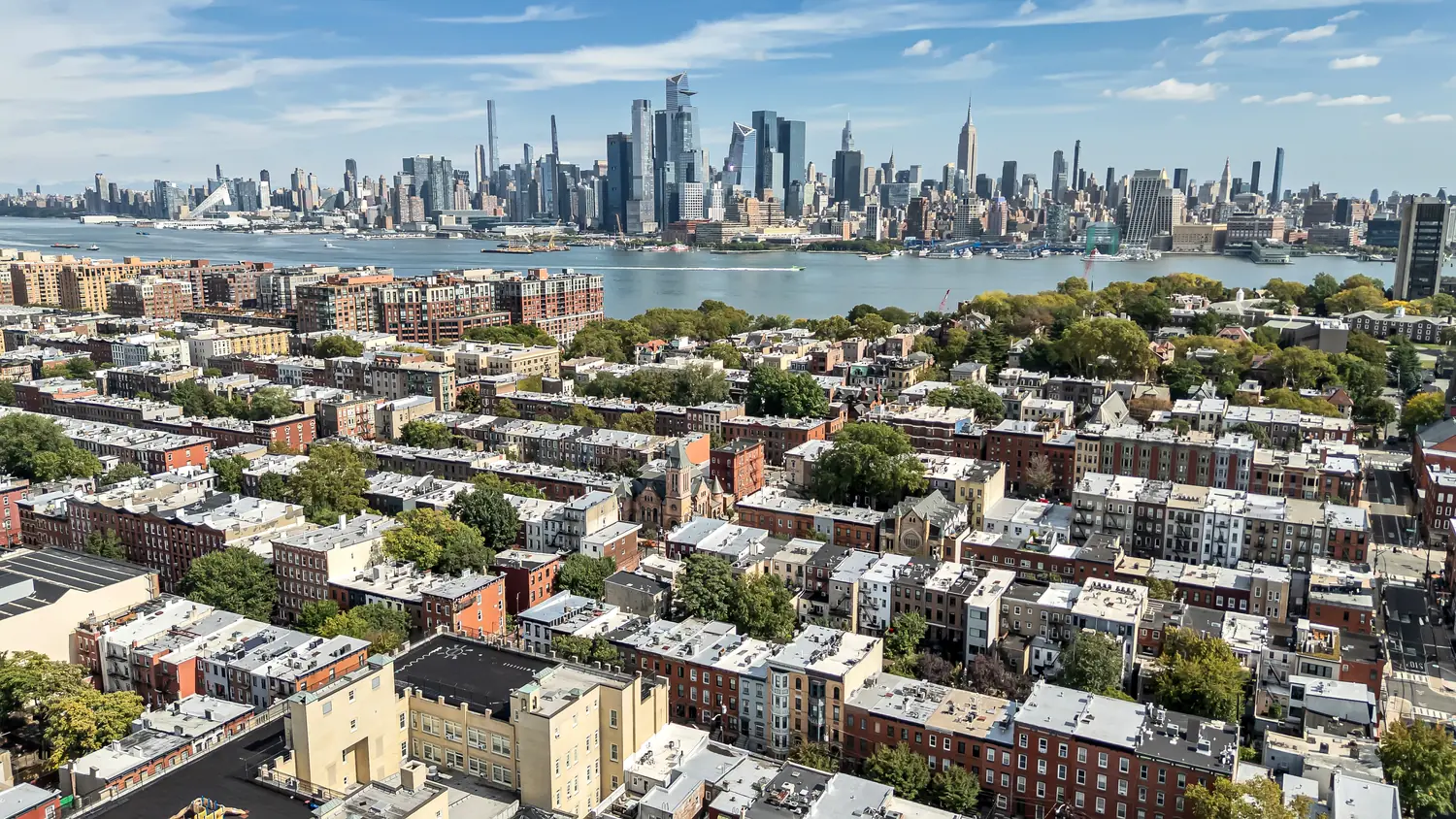 Aerial view across Uptown Hoboken rooftops toward the Hudson River and the Midtown skyline, including the Empire State Building, above the patio at 829 Garden Street.